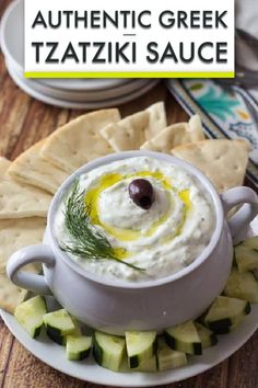 a white bowl filled with tzatzki sauce on top of crackers and cucumbers