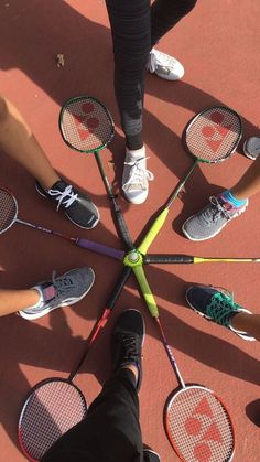 several people standing in a circle holding tennis rackets and shoes on the ground with their feet propped up