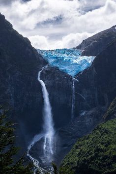 a very tall waterfall in the middle of some mountains with water coming out of it