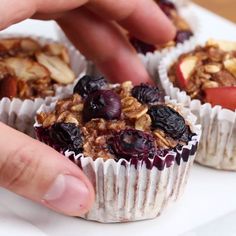 a person picking up some fruit and granola muffins on a white plate