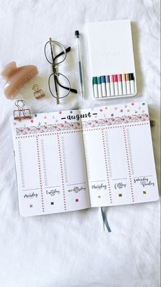 an open planner with markers, pencils and eyeglasses next to it on a bed