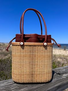 Handwoven Nantucket Lightship Basket Tote bag made by Abby Fisher. Tote features three sizes of staves in maple and cherry creating a stripe pattern on the front and back of the bag. The base and rim are made of maple and there are two Cherry inlays, one on the front of the rim and one along the top. The handles are 18” in leather to match the removable leather liner. The hydrangea charm is optional and can be purchased separately. Each piece has a logo button on the bottom of the bag with scrimshaw noting the year the bag was made and signature of artist, Abby Fisher. Bag dimensions are 8” tall, 8.5” long across the top, and 4” wide. This heirloom piece will last a lifetime and as in the traditional Nantucket custom,can be past down to future generations. Please allow 6-8 weeks for produc Lightship Basket, Nantucket Basket, Nantucket Baskets, Basket Tote, 8 Weeks, Accessories Necklace, Nantucket, Basket Weaving, Stripes Pattern