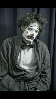 a man with clown makeup sitting in front of a black curtain and wearing a white face paint