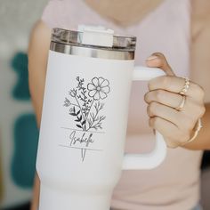 a woman holding a white coffee cup with flowers on it