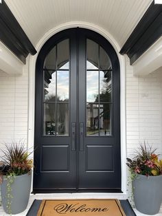 a welcome mat is placed in front of a door with two potted plants on it