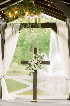 a cross with flowers and greenery on it in front of a large window at a wedding