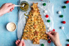 two hands are decorating a christmas tree made out of food on a sheet of paper