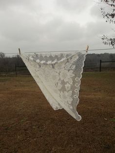 an old lace doily hangs on a clothesline in a field near a barbed wire fence