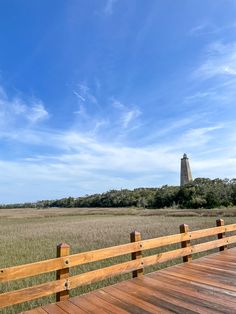 a wooden walkway leading to a light house in the middle of an open field with tall grass