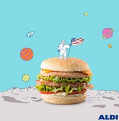 a hamburger with an american flag on top and astronaut in the background, against a blue backdrop