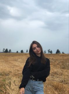 a woman standing in the middle of a field with her arms crossed and looking at the camera