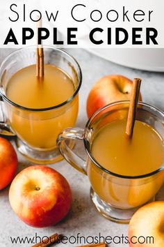 two mugs filled with apple cider sitting next to apples