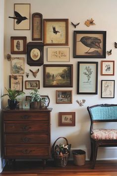 there are many framed pictures on the wall next to a dresser and chair in this room