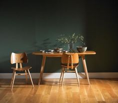 a wooden table with two chairs in front of it on a hard wood floor next to a green wall