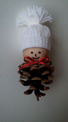 a pine cone ornament with a white knitted hat and red ribbon