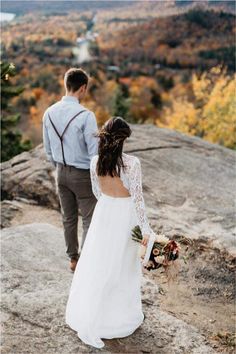 a bride and groom standing on top of a mountain looking out at the valley below