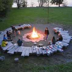 several people sitting around a fire pit in the middle of a field with picnic tables