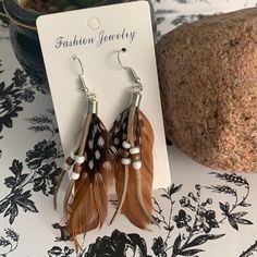 the earrings are brown and white feathers with beads on them, sitting next to a rock