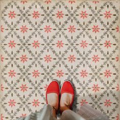 a person wearing red shoes standing in front of a wallpapered floor with flowers