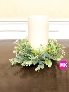 a white candle sitting on top of a wooden table next to green leaves and plants