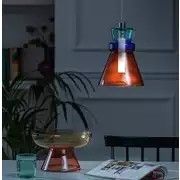 an orange and blue lamp hanging over a dining room table next to a magazine on a chair