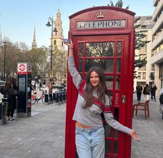 a woman standing in front of a red phone booth with her arms up and smiling