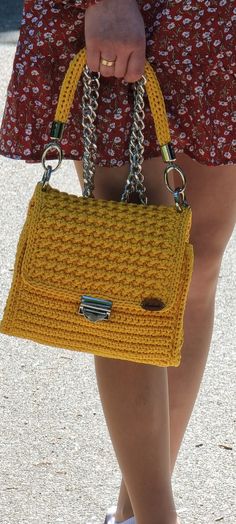 a close up of a person holding a yellow purse with chains on it's handles