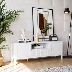 a living room with white furniture and plants on the sideboard in front of a large mirror