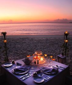 a table set up on the beach with candles and plates in front of an ocean view