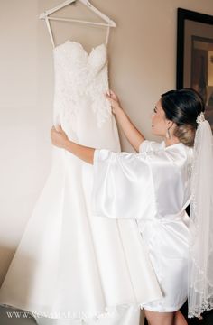 the bride is trying on her wedding dress in front of the bridal gown hanger