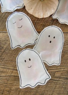 three ghost shaped paper plates sitting on top of a wooden table next to a pumpkin