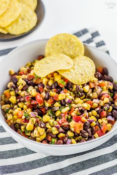 a white bowl filled with black beans and corn next to tortilla chips on a striped table cloth