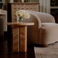 a vase with white flowers sitting on top of a wooden table next to a chair