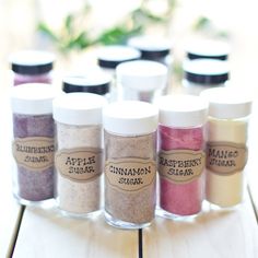 seven jars filled with different colored sand on top of a wooden table