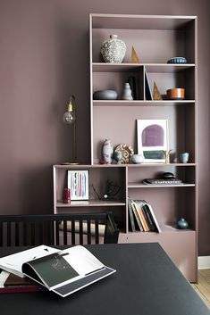 an open book shelf in the corner of a room with purple walls and black table