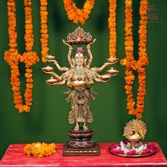 there is a golden statue on top of a red table with orange flowers around it