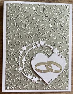 a handmade card with two wedding rings and a heart on the front, sitting on top of a wooden table