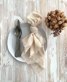 a white plate topped with two napkins next to a vase filled with dried flowers