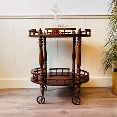 a wooden serving cart with wheels on the floor next to a potted plant