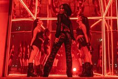 three women standing in front of a window with red light behind them and one woman wearing black