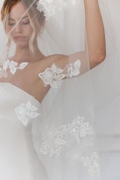 a woman wearing a wedding veil with white flowers on the side and her hair comb in her hand