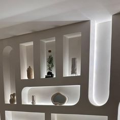 a room with several shelves and vases on the wall, all lit up by lights