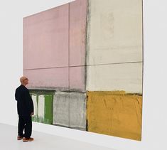 a man standing in front of a large painting on the side of a white wall