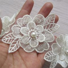 two white flower brooches with pearls in the middle and one being held by someone's hand