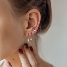 This stacking set features 3 different earrings, all made from 18 karat gold-plated sterling silver. It has: ✅ One small huggie hoop earring with a single, clear-coloured, Baguette-cut zircon stone in a four-prong setting hanging from its lower edge;  ✅ One small huggie hoop earring with a small flower-shaped pendant, which is decorated with four round, clear-coloured zircon stones, and  ✅ One small stud earring with two clear-coloured, oval-shaped zircon stones arranged in a V-shape, with a but Dainty Hoop Earrings, Stacked Earrings, Ear Stack, Hoop Earring Sets, Small Earrings Studs, Delicate Earrings, Baguette Cut, Single Earring, Jewelry Inspo