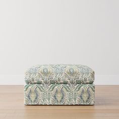 an upholstered footstool on the floor in front of a white wall