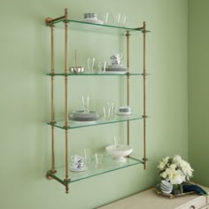 the shelves are filled with glassware and vases on top of each shelf in front of a green wall