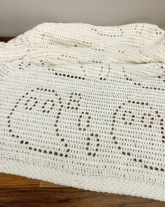 a white crocheted blanket with the word love written on it, laying on top of a wooden floor