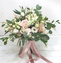 a bouquet of flowers with pink ribbon tied around it on a white wooden wall background