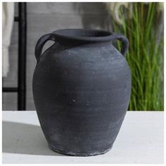 a black vase sitting on top of a white table next to a green grass plant